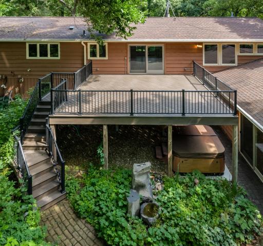 A large elevated maintenance-free deck overlooks a serene backyard retreat, surrounded by mature trees, privacy, and cleared paths.