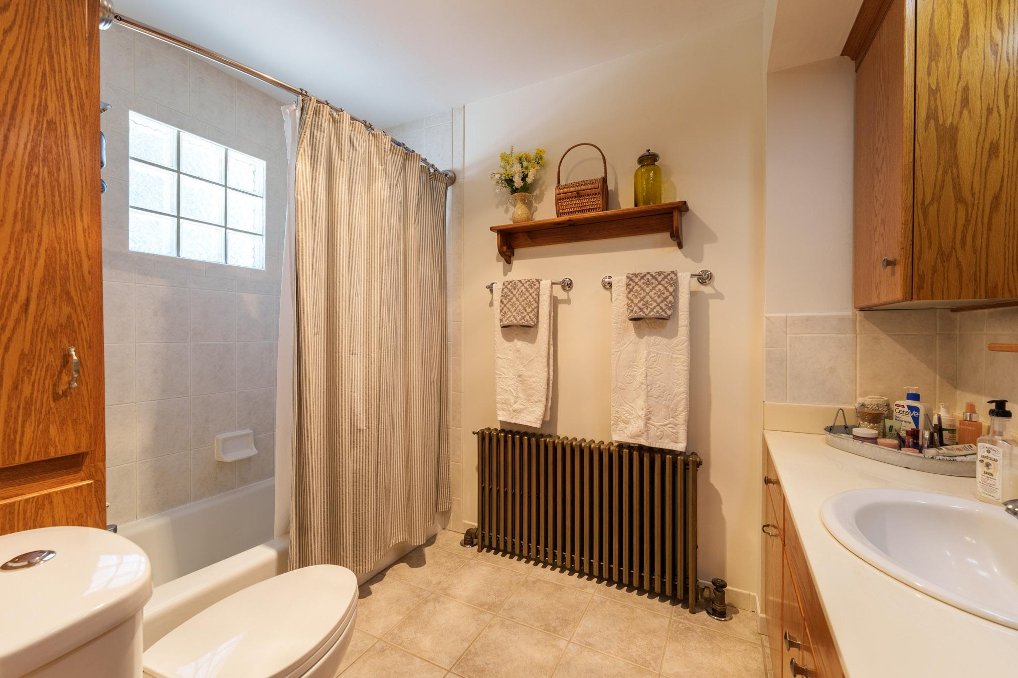 The main floor full-bath features a small linen closet to the left and a glass-block window as part of the shower /tub surround.