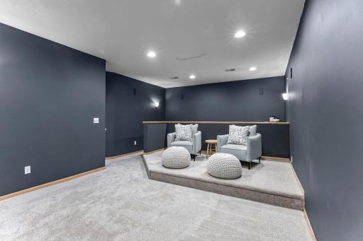 A dedicated theater room with tiered flooring, wall scones, and speaker hook-ups.