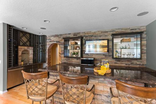 The showstopping custom wet bar features rich stone accents, a center island, beverage refrigerators, dishwasher, and microwave.
