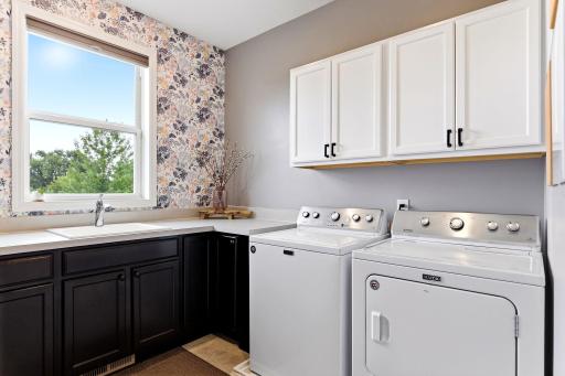 Floral wallpaper turns laundry day pleasant, with a utility sink, folding counter, and cabinets on duty.