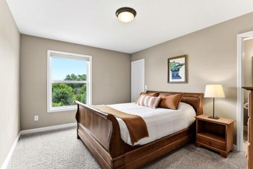 A serene guest primary suite in soft neutrals with peaceful wooded and pond views.