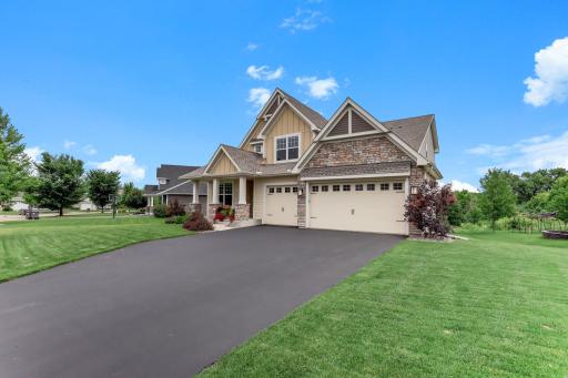 A sweeping driveway leads to the three-car garage, framed by manicured lawn and fresh landscaping.