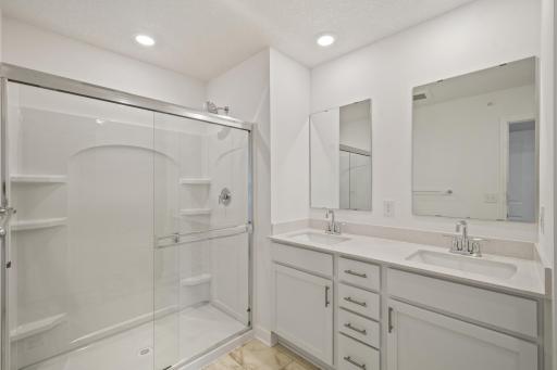 (Photo of an inventory home, actual homes finishes will vary) The primary bedroom features an en suite bathroom with a dual sink vanity, quartz countertops, and glass door shower.