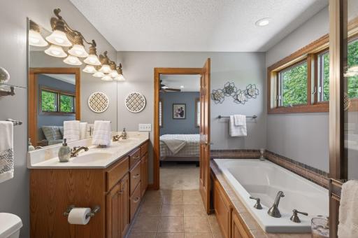 Private bathroom in primary suite with dual sinks, glass shower, and a jacuzzi tub