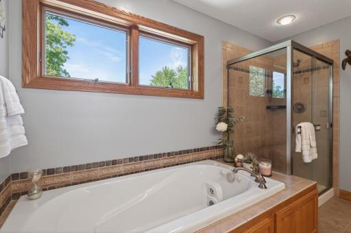 Private bathroom in primary suite with dual sinks, glass shower, and a jacuzzi tub