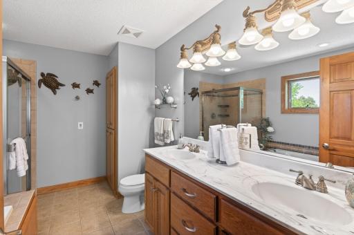 Private bathroom in primary suite with dual sinks, glass shower, and a jacuzzi tub