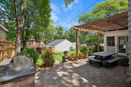 Large, fully fenced backyard features a new paver patio and walkway, pergola, and built-in grill with stone countertops.