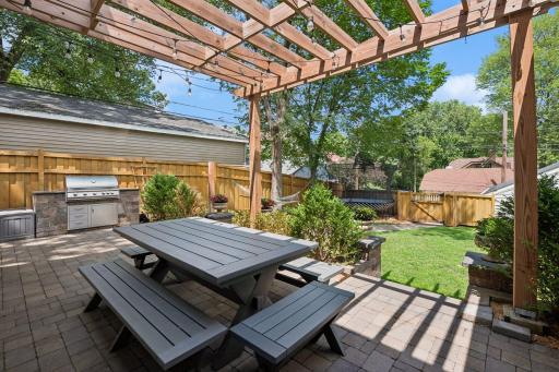 Large, fully fenced backyard features a new paver patio and walkway, pergola, and built-in grill with stone countertops.