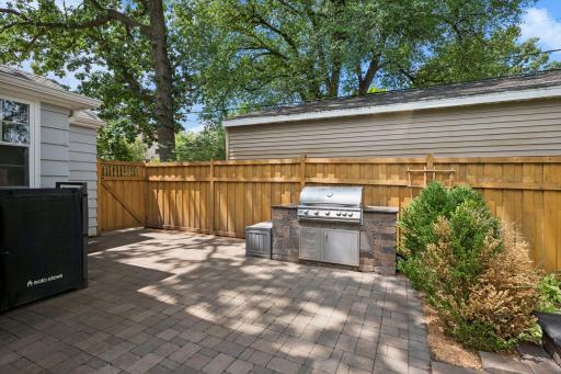 Large, fully fenced backyard features a new paver patio and walkway, pergola, and built-in grill with stone countertops.