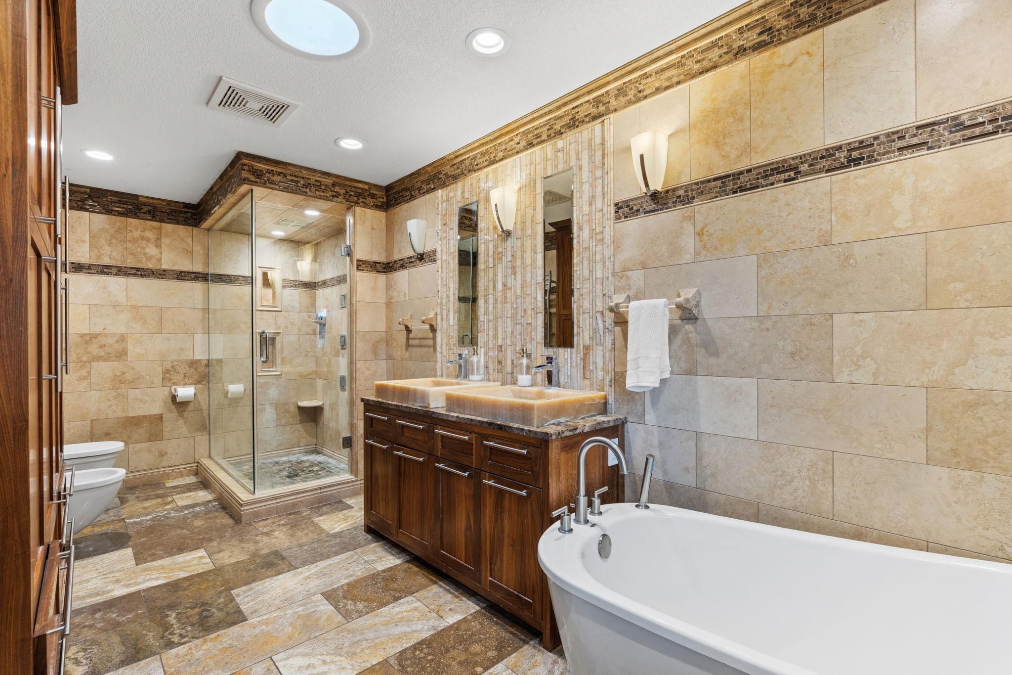 The primary bathroom with double vanity, sink in tub, freestanding shower, towel warmer, and linen storage.
