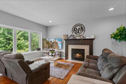 The living room is filled with natural light from large windows and features a gas fireplace with a tile surround.