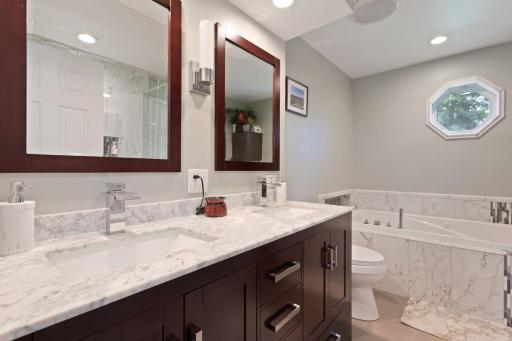 Remodeled in 2018, the upper level walk-through bath featuring a jacuzzi-style tub with built-in heater, double vanity with granite top and soft close cabinetry, tiled flooring, and recessed lighting for a clean, modern spa-like feel.