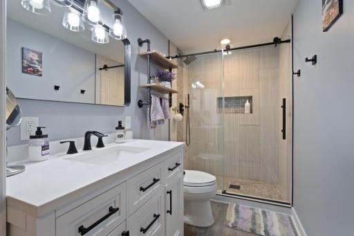 The lower level 3/4 bathroom fully remodeled in 2021 and showcases a modern, spa like design. It features luxury vinyl plank flooring, a beautifully tiled walk-in shower with glass enclosure, quartz-topped vanity and a recessed shampoo niche.