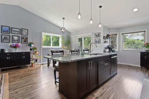 The sun-splashed dining room open to the kitchen with vaulted ceilings and luxury vinyl plank flooring. Sliding door leads to the updated maintenance free deck, creating an easy indoor-outdoor flow perfect for entertaining and everyday living.