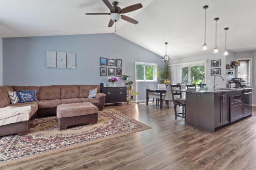 Wide angle of the light and bright open concept where the kitchen, dining room, and living room flow seamlessly together. Vaulted ceilings and luxury vinyl plank flooring create an airy, spacious feel filled with natural light throughout.