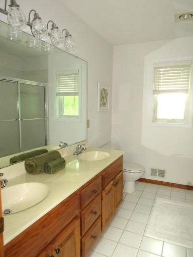 The upper level full bath has dual sinks, white ceramic tiled flooring, updated light globes and fresh paint.
