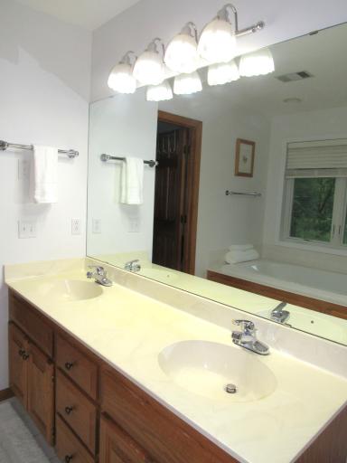 Primary bath vanity with dual sinks, white ceramic tiled flooring and linen center.