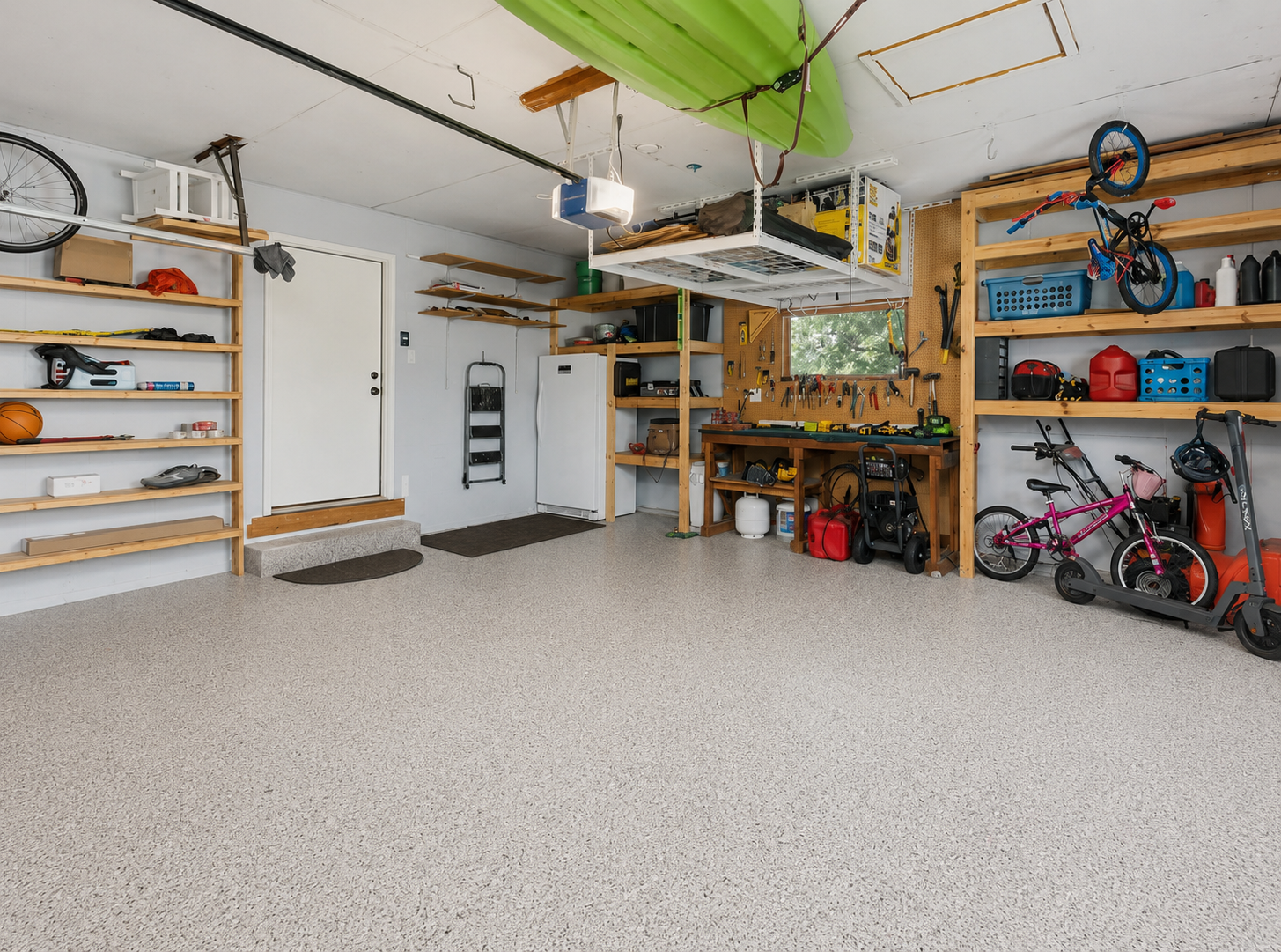 Clean, organized garage with durable floor coating, wall-mounted storage, and workbench. (Current photo as been AI edited to show the recent flooring improvements.)
