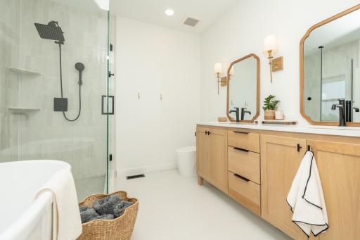 Luxurious ensuite featuring a double vanity, custom cabinetry, and a walk-in tiled shower