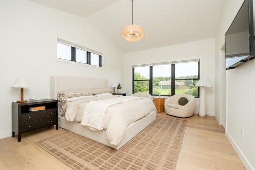 Bright primary suite featuring vaulted ceilings, oversized windows, and peaceful backyard views