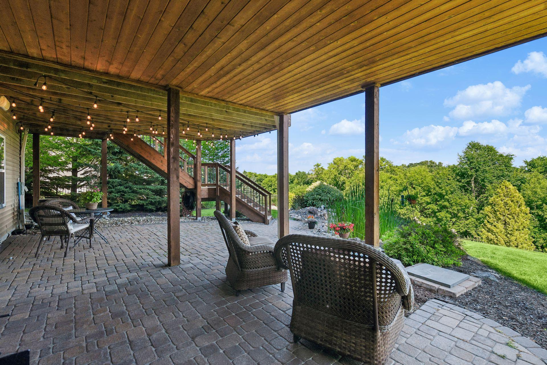 Covered lower patio with paver flooring and overhead string lighting, set beneath the upper deck.