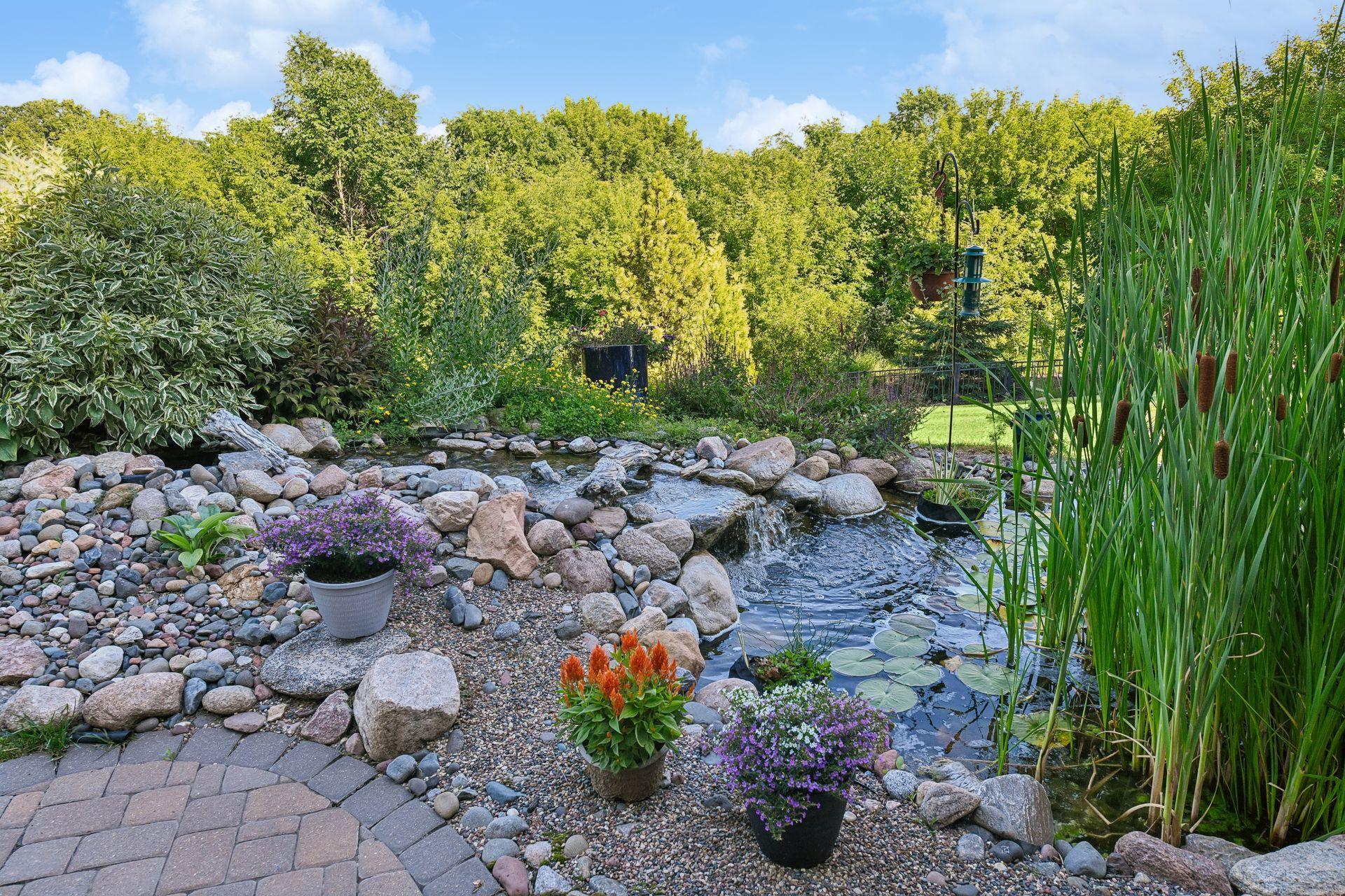 Landscaped stone waterfall pond bordered by boulders and plantings.