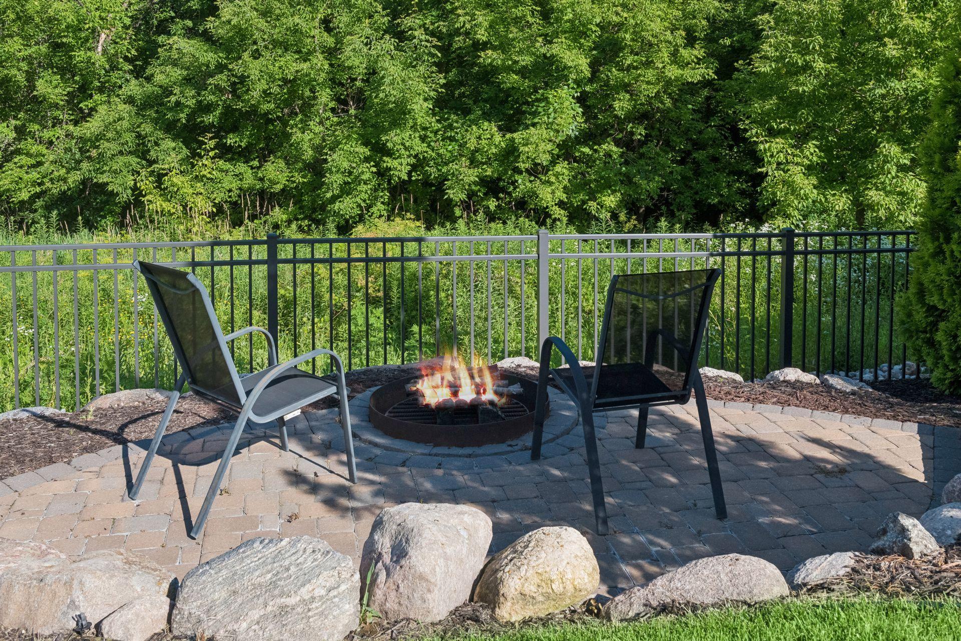 Stone wood-burning fire pit within the fully fenced black aluminum backyard.