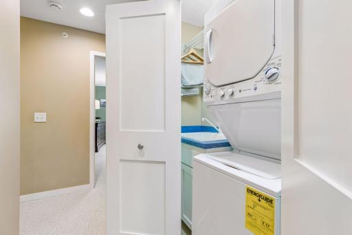 The laundry closet features a stackable washer & dryer and deep utility/laundry sink. Cabinetry and work surfaces flank both sides of the washer and dryer.