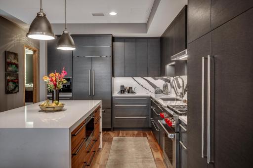 The chefâs kitchen features a striking waterfall island with seating, Cambria countertops and statement backsplash, Wolf and Sub-Zero appliances, Miele built-in coffee maker, and gorgeous custom cabinetry.