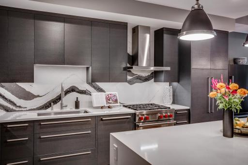 The chefâs kitchen features a striking waterfall island with seating, Cambria countertops and statement backsplash, Wolf and Sub-Zero appliances, Miele built-in coffee maker, and gorgeous custom cabinetry.