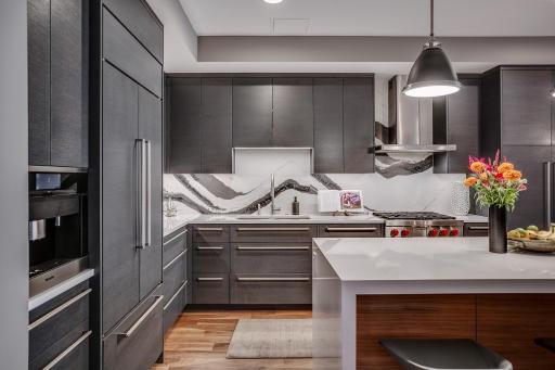 The chefâs kitchen features a striking waterfall island with seating, Cambria countertops and statement backsplash, Wolf and Sub-Zero appliances, Miele built-in coffee maker, and gorgeous custom cabinetry.