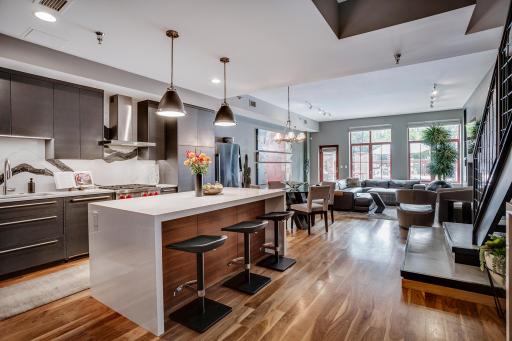 The interior architecture makes an immediate impression with oversized windows, tall ceilings, a sleek media wall, fireplace, and a modern iron and concrete staircase, a nod to the areaâs industrial history.