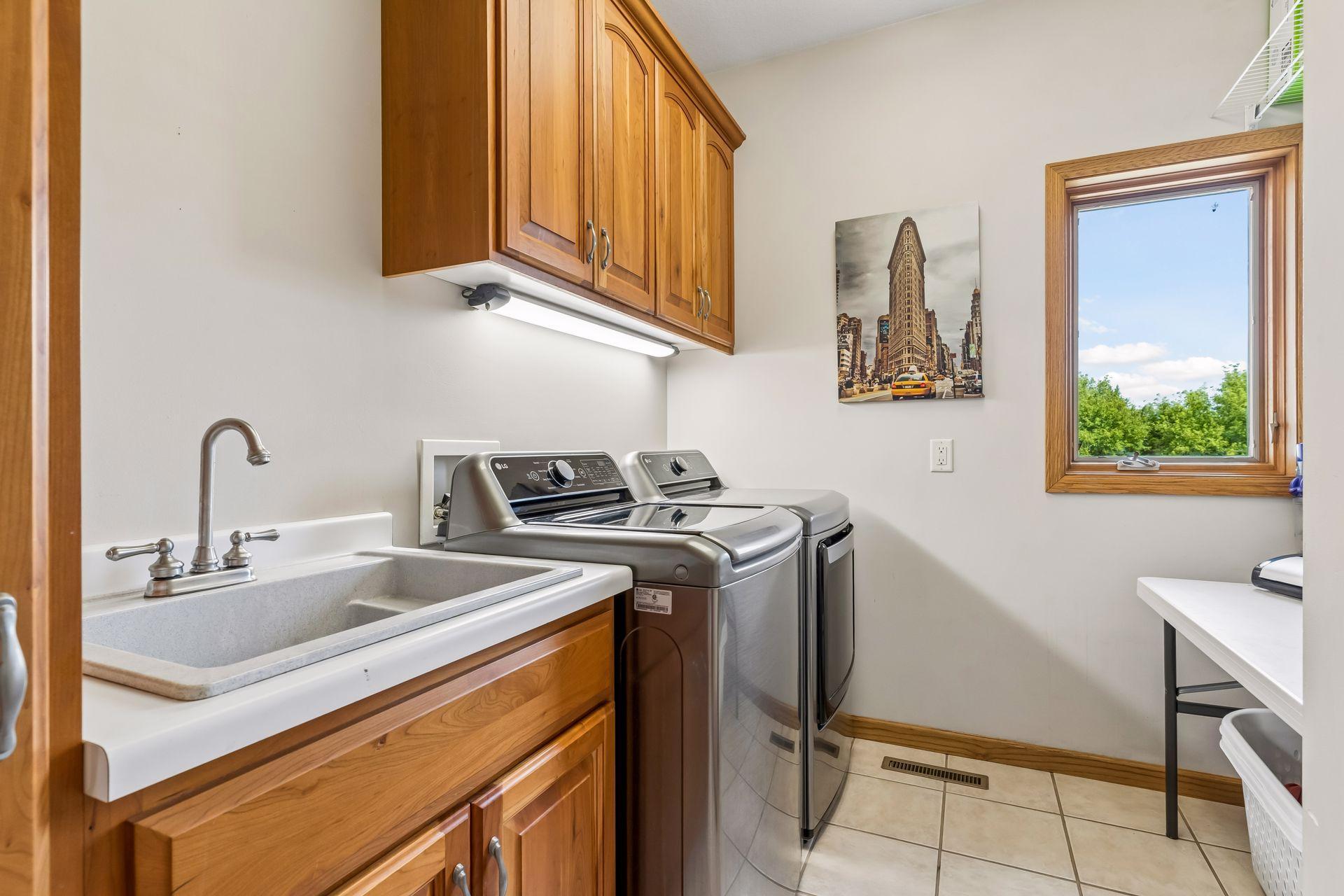 The thoughtfully designed main-level laundry provides a functional workspace with a utility sink, durable tile flooring, overhead lighting, nice window and extensive storage solutions.