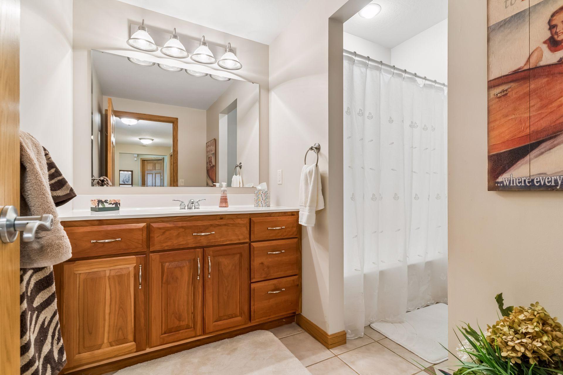 The lower-level full bath showcases heated tile flooring, a well-appointed vanity, tub/shower combination, overhead lighting, and thoughtful storage options.