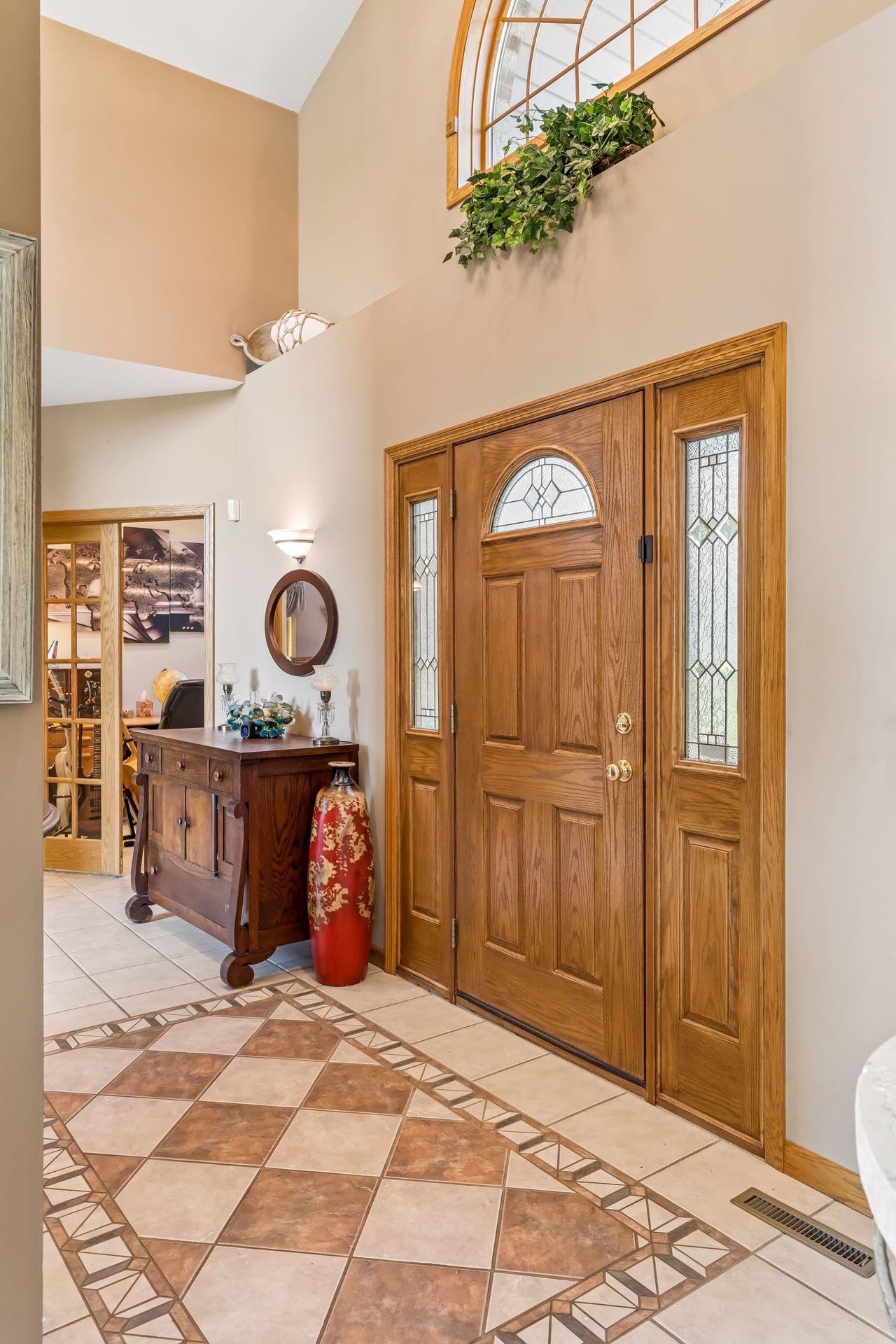 The impressive foyer makes a memorable first impression with tile flooring, a beautiful transom window, chandelier lighting, a convenient coat closet, and soaring 16-foot ceilings.