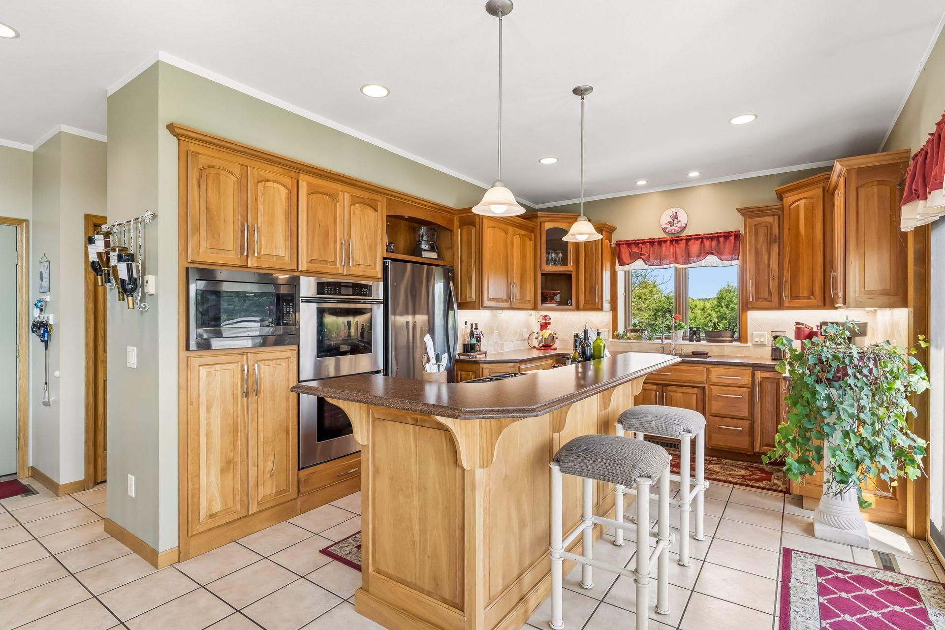 A beautifully appointed kitchen showcases rich cherry wood cabinetry, heated tile flooring, a decorative tile backsplash, Silestone countertops, pendant and overhead lighting, breakfast bar, and an abundance of cabinetry for exceptional storage.