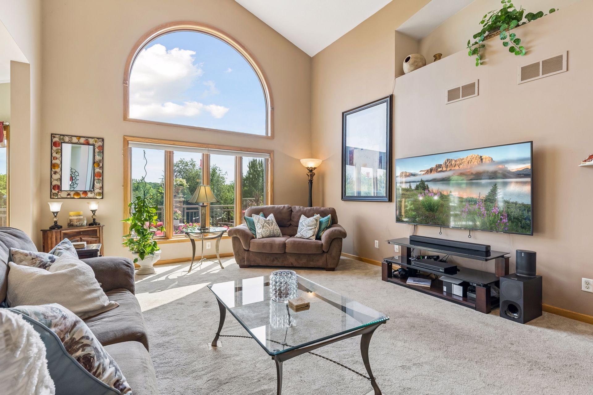The stunning living room showcases impressive ceiling height, abundant windows, and a comfortable blend of soft carpeting, overhead lighting, and a ceiling fan, creating a bright and welcoming gathering space.