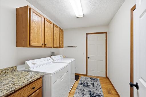 Convenient main-level laundry room featuring granite countertops, abundant cabinetry, hardwood floors, and plenty of space for laundry, storage, and everyday organization.