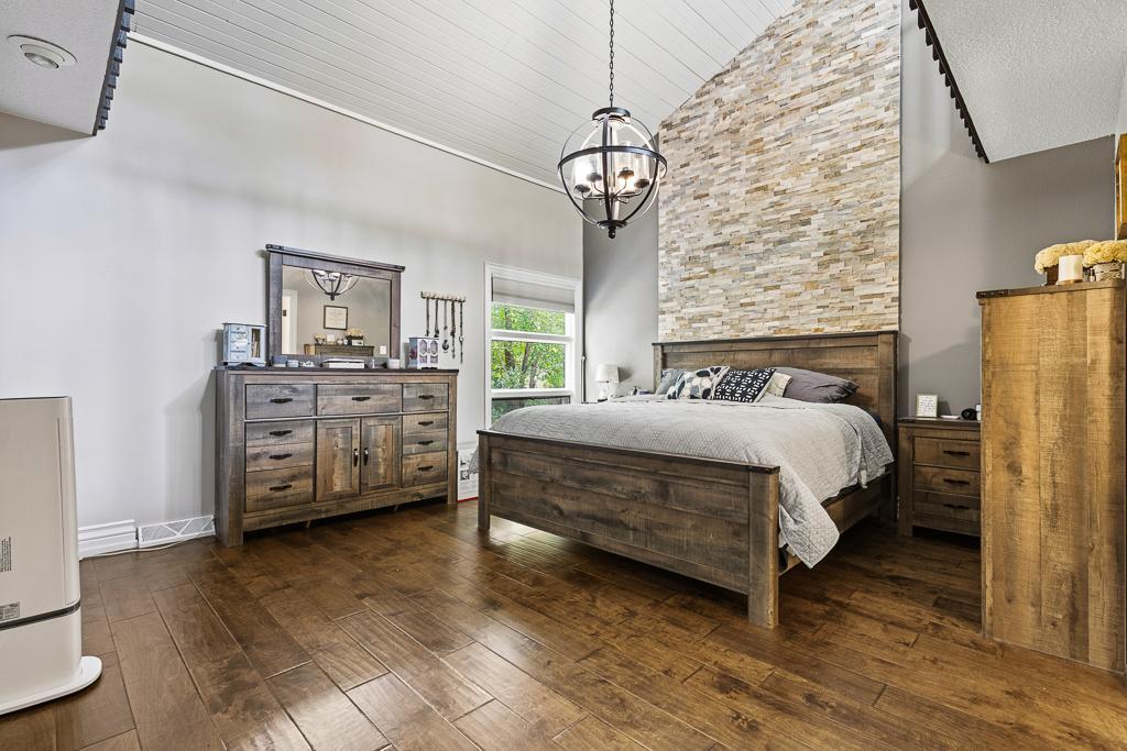 Showstopping primary bedroom with vaulted ceiling, 3/4 bath ensuite, hanging light fixture, dual closets, stone wall accent, and a spacious private loft