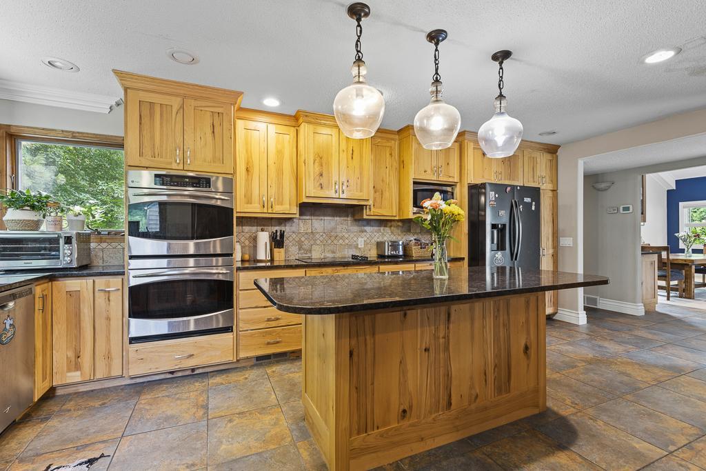 Can't get enough of the beautiful kitchen - stainless steel appliances, double wall oven, tiled backsplash, recessed lighting, and 3 hanging light fixtures to highlight the center island