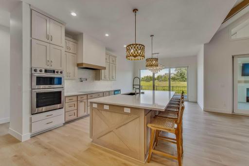 Spacious gourmet kitchen offering an expansive center island with seating, abundant custom cabinetry, and picturesque views through the dining area. (Virtually staged photo)