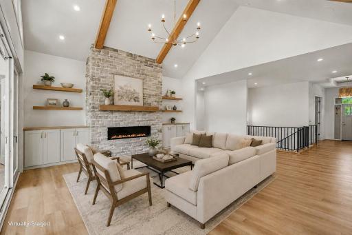 Spectacular great room featuring a floor-to-ceiling stone fireplace, custom floating shelves, and vaulted ceilings. (Virtually staged photo)