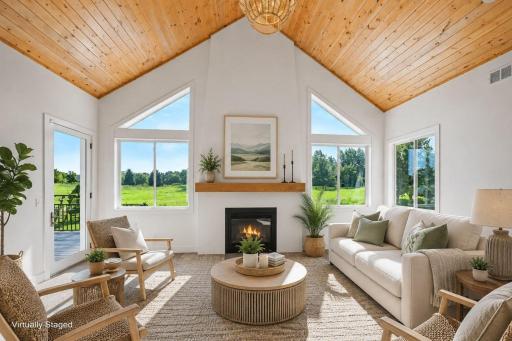 Warm and welcoming gathering space centered around a cozy fireplace, soaring wood-planked vaulted ceiling, and expansive windows overlooking picturesque views. (Virtually staged photo)