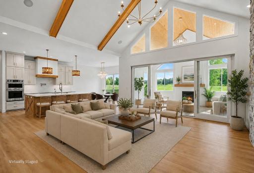 Bright and inviting great room showcasing dramatic two-story windows, vaulted ceilings with architectural beams, and effortless indoor-outdoor living. (Virtually staged photo)