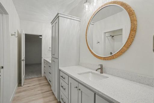 Bright shared bathroom featuring quartz countertops, custom cabinetry, designer lighting, and abundant linen storage.