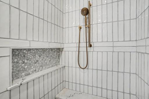 Luxurious walk-in shower showcasing floor-to-ceiling designer tile, a built-in bench, decorative mosaic accent, and premium fixtures.