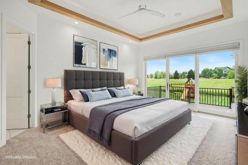 Luxurious main-level owner's suite featuring a tray ceiling with wood beam accents, expansive windows, and a peaceful retreat overlooking the backyard.(Virtually staged photo)
