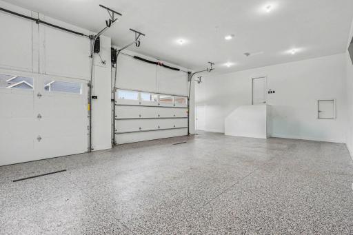 Finished four-car garage featuring durable epoxy flooring, high ceilings, oversized doors, and room for hobbies, workshop space, or additional storage.