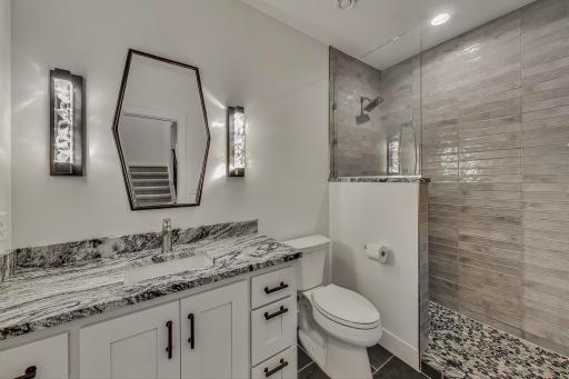 Beautifully finished lower-level bathroom with granite countertops, custom cabinetry, designer lighting, and a tiled walk-in shower